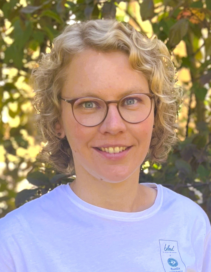 Eine Person mit lockigem blondem Haar vor grüner Gartenlandschaft