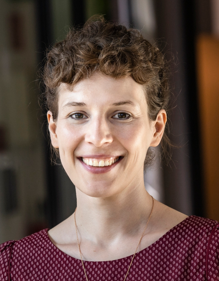 Portrait einer Frau mit curly Haar, Bluse mit Muster, schulterfreier Blick.
