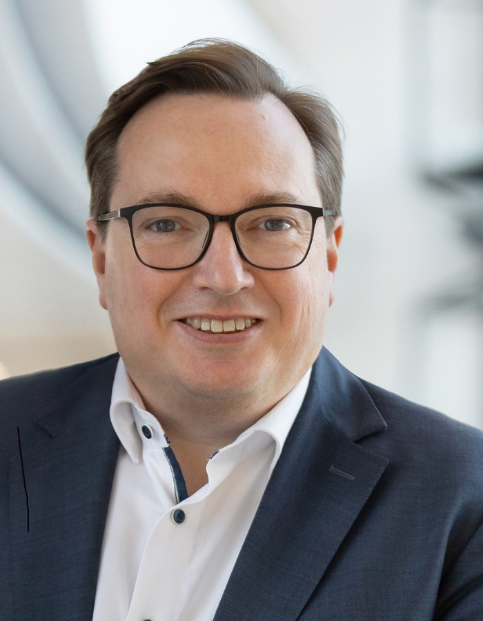 Mann mit weißem Hemd, dunkelblauem Sakko und schwarzer Brille