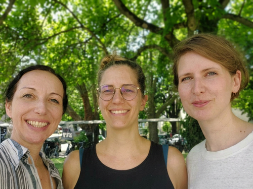 Drei lächelnde Frauen vor einem grünen Hintergrund aus Bäumen.