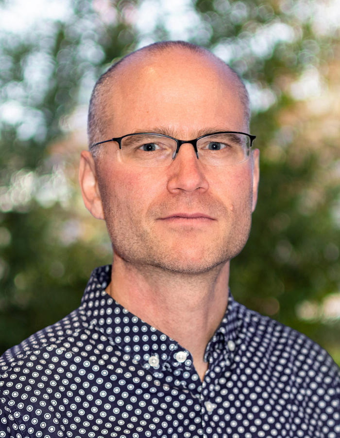 Arnim Wiek mit gemustertem Hemd vor unscharfem, grünem Hintergrund im Freien.