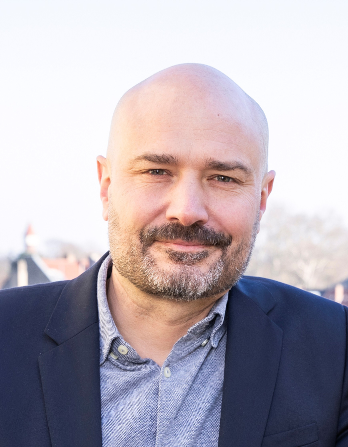 Daniel Lang trägt Sakko und Hemd vor unscharfem Außenhintergrund.