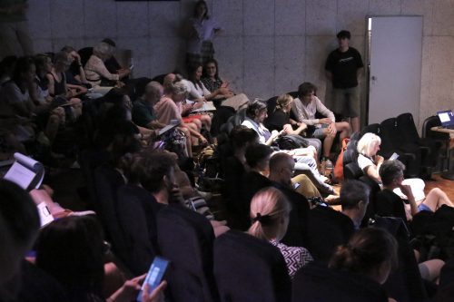 Publikum in einem Saal beim Ausfüllen von Fragebögen