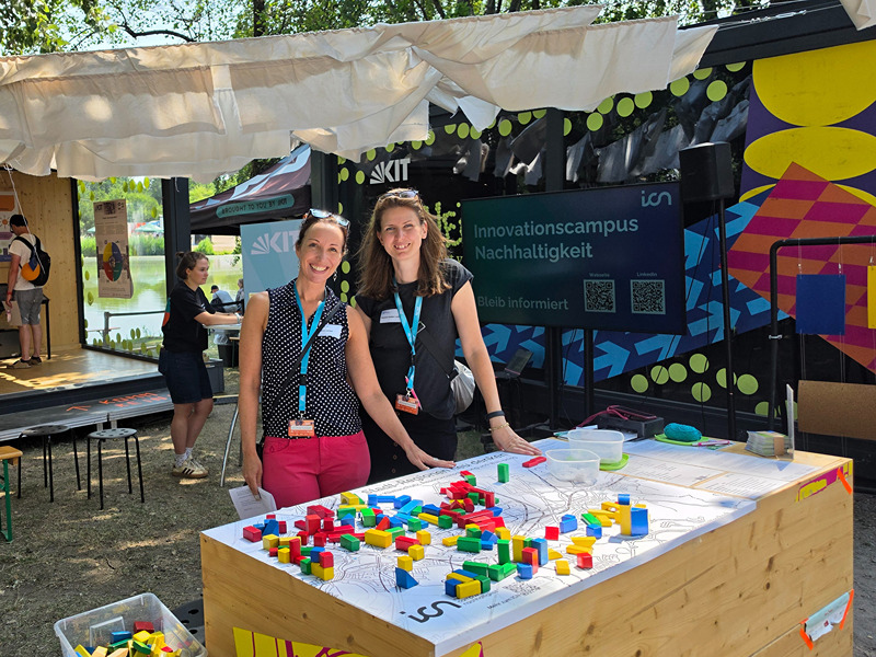 Zwei Frauen an einem Stand des Innovationscampus Nachhaltigkeit mit einem Mitmachangebot aus bunten Klötzen.