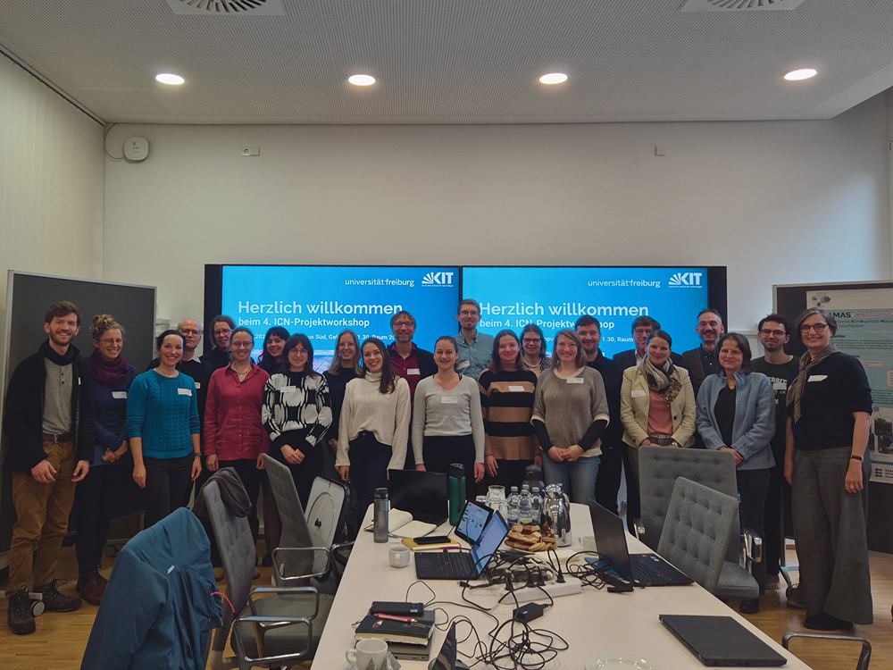 viele Personen stehen vor einem Bildschirm mit der Aufschrift "herzlich willkommen zum 4. Projektworkshop des Innovationscampus Nachhaltigkeit"